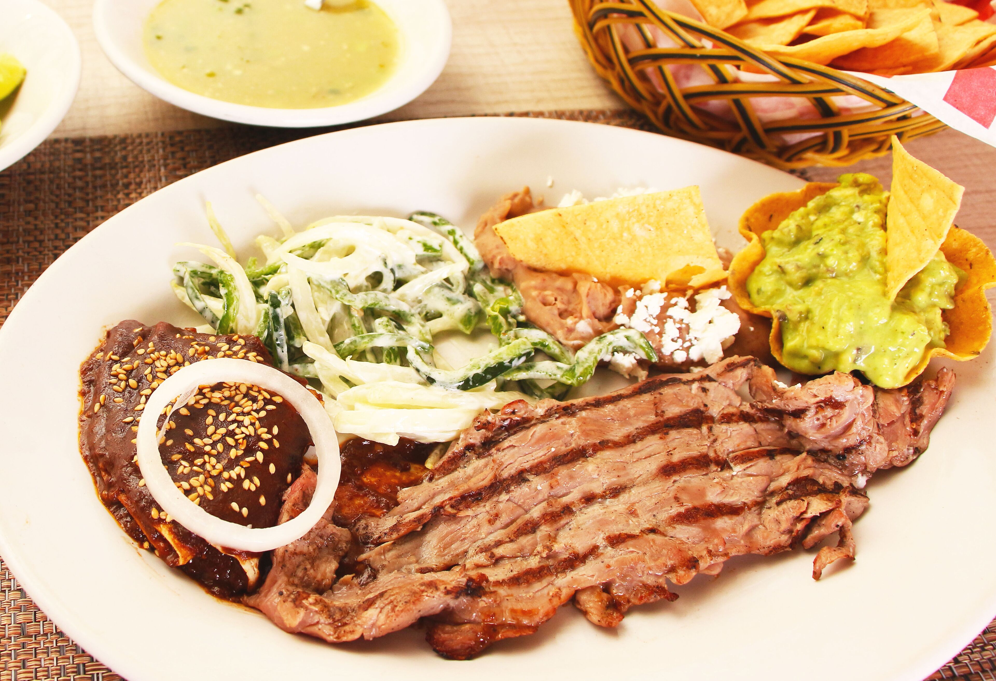 A plate of food with grilled meat, guacamole, and a side salad.