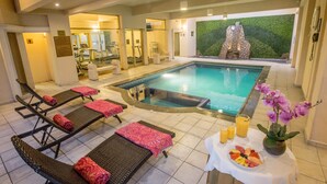 Zona de piscina con sillones de descanso, un jacuzzi y una mesa con frutas y bebidas.