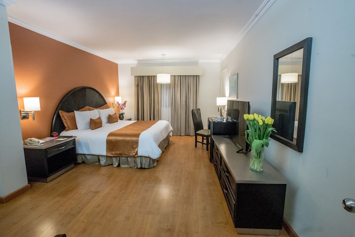 Een hotelkamer met een groot bed, een bureau, een stoel, een spiegel en een bloemenvaas.