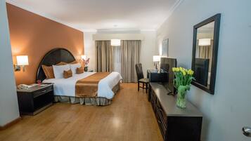 Habitación de hotel con una cama grande, un escritorio, una silla, un espejo y un florero con flores.