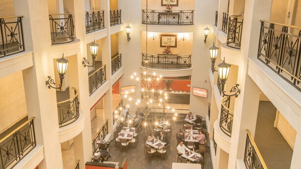 Un vestíbulo de hotel de varios niveles con zonas de comedor, candelabros y una escalera central.