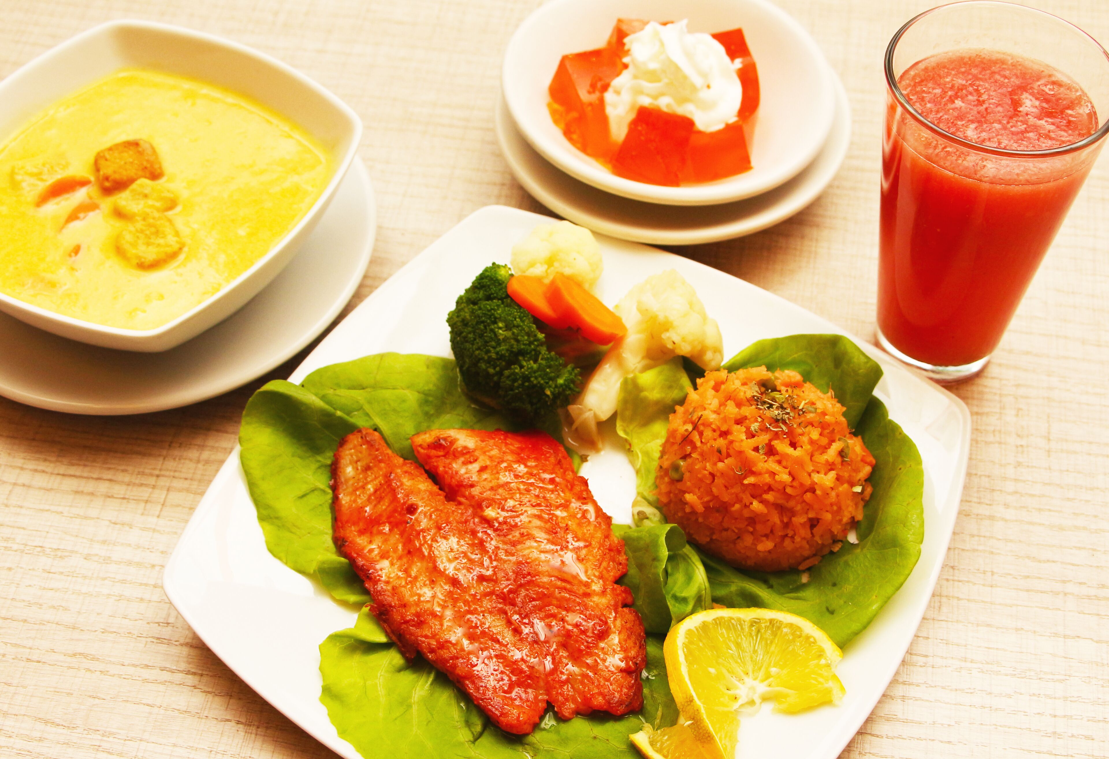A plate with grilled fish, rice, vegetables, and a glass of juice.
