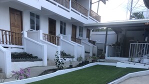 Um edifício residencial com um gramado bem cuidado, paredes externas brancas e varandas de madeira.
