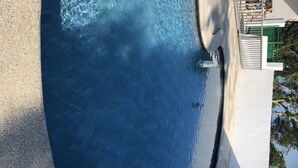 Uma piscina com água azul cristalina, um deck de concreto e uma cerca de metal.