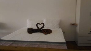 Uma cama com arranjo de toalha em formato de coração, uma parede branca lisa e uma mesinha de cabeceira de madeira com um livro.