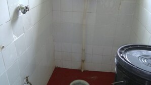 A small, tiled bathroom with a toilet, a bucket, and a black barrel. - Koyucho Guest House (Bondo)