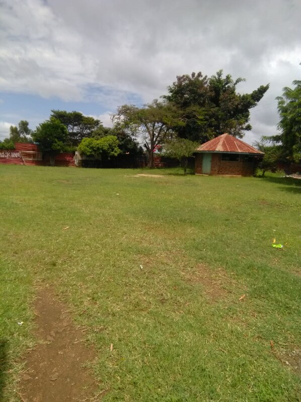 A grassy outdoor area with a small brick building and trees.