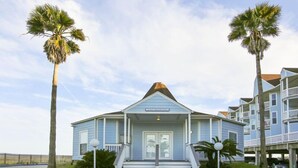 A small, light blue building with a gabled roof and a porch, surrounded by palm trees.
