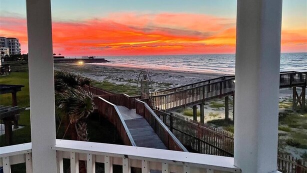 A wooden boardwalk leading to a beach with a sunset view.