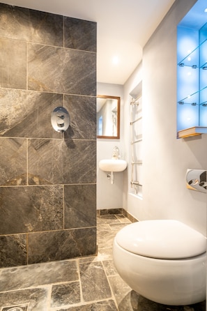 A bathroom with a white toilet, a sink, and a shower area with a glass-enclosed shower. - Murphys place (Bath)