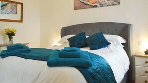 Uma cama bem arrumada com cabeceira estofada cinza, roupa de cama branca e mantas azuis-esverdeadas.