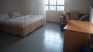 A bedroom with a bed covered by a mosquito net, a window with bars, a desk, and a chair.