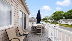 Une terrasse en bois avec une table et des chaises, un parasol et une rambarde blanche.