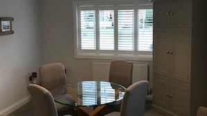 Comedor con mesa de vidrio, cuatro sillas, lámpara colgante, ventana con persianas y un armario.