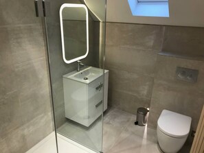 Un baño moderno con ducha de vidrio, lavamanos blanco y retrete.