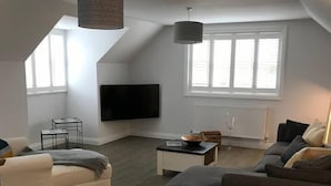 Una sala de estar moderna con un televisor de pantalla plana, dos sofás, una mesa de centro y una mesa de comedor.