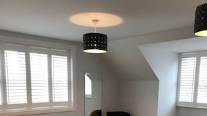 Un dormitorio con cama, mesita de noche, silla, espejo y ventana con persianas.