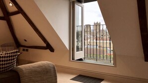Un dormitorio tipo loft moderno con techo inclinado, un ventanal con vistas a un edificio histórico y un pequeño balcón.