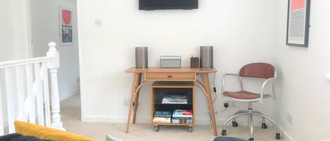 A living room with a TV mounted on the wall, a wooden desk with a chair, and a bookshelf.