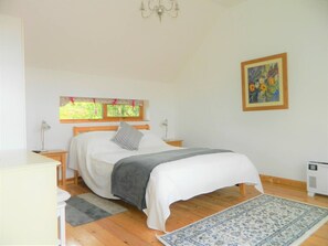 Une chambre à coucher comprenant un lit, une table de chevet, une lampe, une fenêtre avec des rideaux, un radiateur et un tableau accroché au mur.