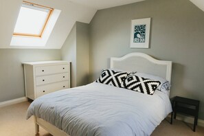 A bedroom with a sloped ceiling, a skylight, a bed with patterned pillows, a white dresser, and a framed sign on the wall. - Family Home in Newquay, Parking, 3 min Walk Beach (Newquay)