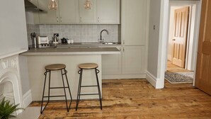 A kitchen with a central island, two bar stools, hanging pendant lights, and a patterned backsplash.