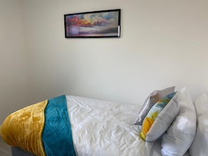 Uma cama com colchão branco, cobertor amarelo e travesseiro com desenho colorido.