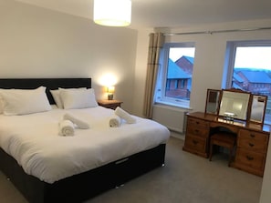 Hotellihuone, jossa on sänky, yöpöytälamppu, lipasto ja ikkuna, josta on näkymä rakennuksiin.