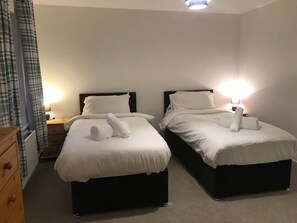 A hotel room with two beds, each with a headboard, bedside tables, and lamps.