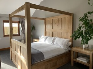 A four-poster bed with a wooden headboard, a bedside table with a lamp, and a plant on the right side. - Abbey View Cottage - Scandi Spa Hot Tub (Chard)