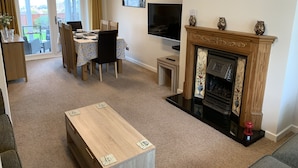 A living room with a fireplace, a dining table, chairs, a TV, and a clock on the wall. - Paignton View Holiday Home (Paignton)