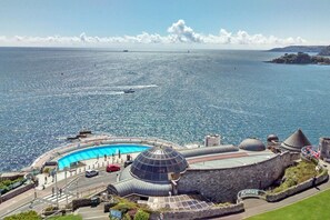 Udsigt over kysten med en swimmingpool, kuppelformede bygninger og en klar himmel.