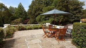 An outdoor patio with stone flooring, wooden furniture, and a green umbrella. - Lakeview Cottage (Ivybridge)