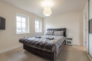 A bedroom with a large bed, two bedside tables, a radiator, and a window. - Stylish & Modern 3 Bedroom Home (Bangor)