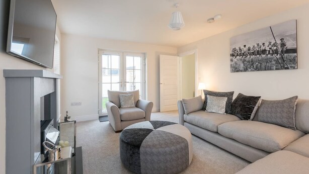 Un salon moderne comprenant un canapé, un fauteuil, un pouf et un téléviseur à écran plat fixé au mur.