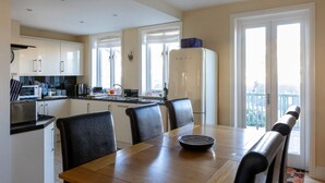 A modern kitchen with white cabinets, a dining table with chairs, and a refrigerator. - Central Dartmouth Townhouse (Dartmouth)