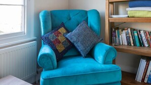 A teal armchair with patterned cushions, a bookshelf with books, a painting, and a mirror. - Central Dartmouth Townhouse (Dartmouth)