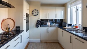 A modern kitchen with white cabinets, a black countertop, a microwave, a stove, and a clock on the wall. - Central Dartmouth Townhouse (Dartmouth)