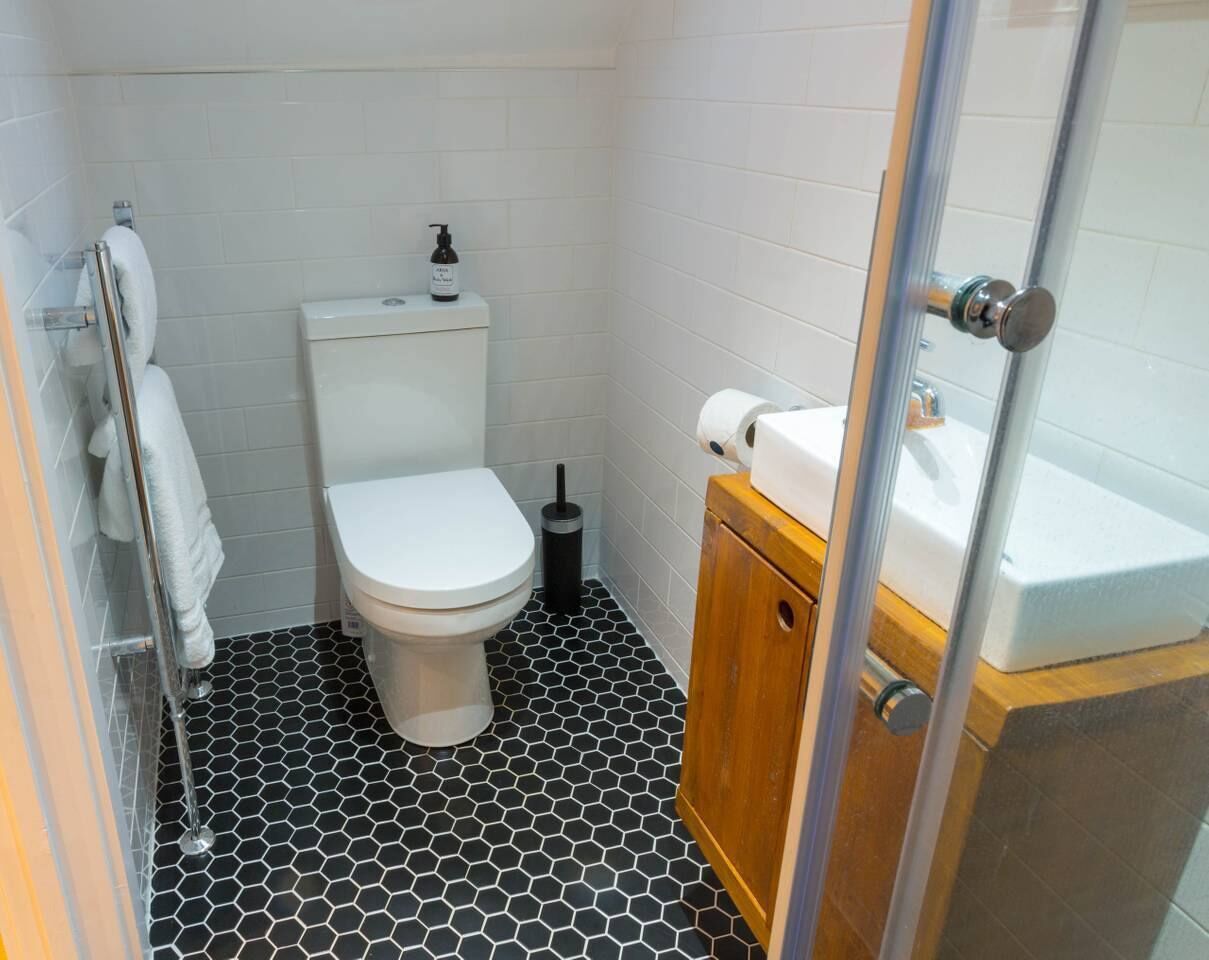 A small, modern bathroom with a white toilet, a wooden cabinet, and a glass shower enclosure.