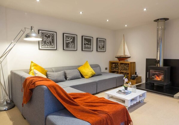 A modern living room with a grey sofa, yellow pillows, a white coffee table, and a wood-burning stove.
