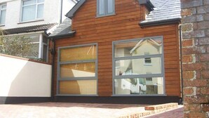 A two-story house with a wooden facade, large windows, and a brick wall on the right. - The Old Stable, Lower Parkstone, Poole (Poole)