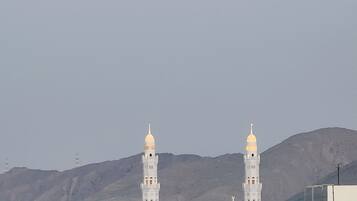 A mosque with two minarets and three domes, set against a mountainous backdrop.