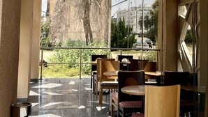 A modern outdoor seating area with a glass wall providing a view of a tree and buildings. - Citadines Al Ghubrah Muscat (Muscat)