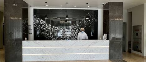 A modern reception desk with a geometric patterned backdrop, a marble counter, and a security camera above.