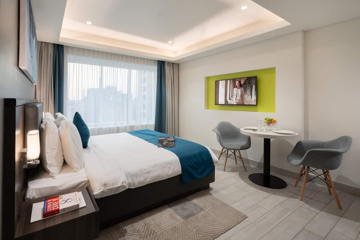 Habitación de hotel moderna con una cama grande, una mesita con sillas, un televisor y un cuadro en la pared.