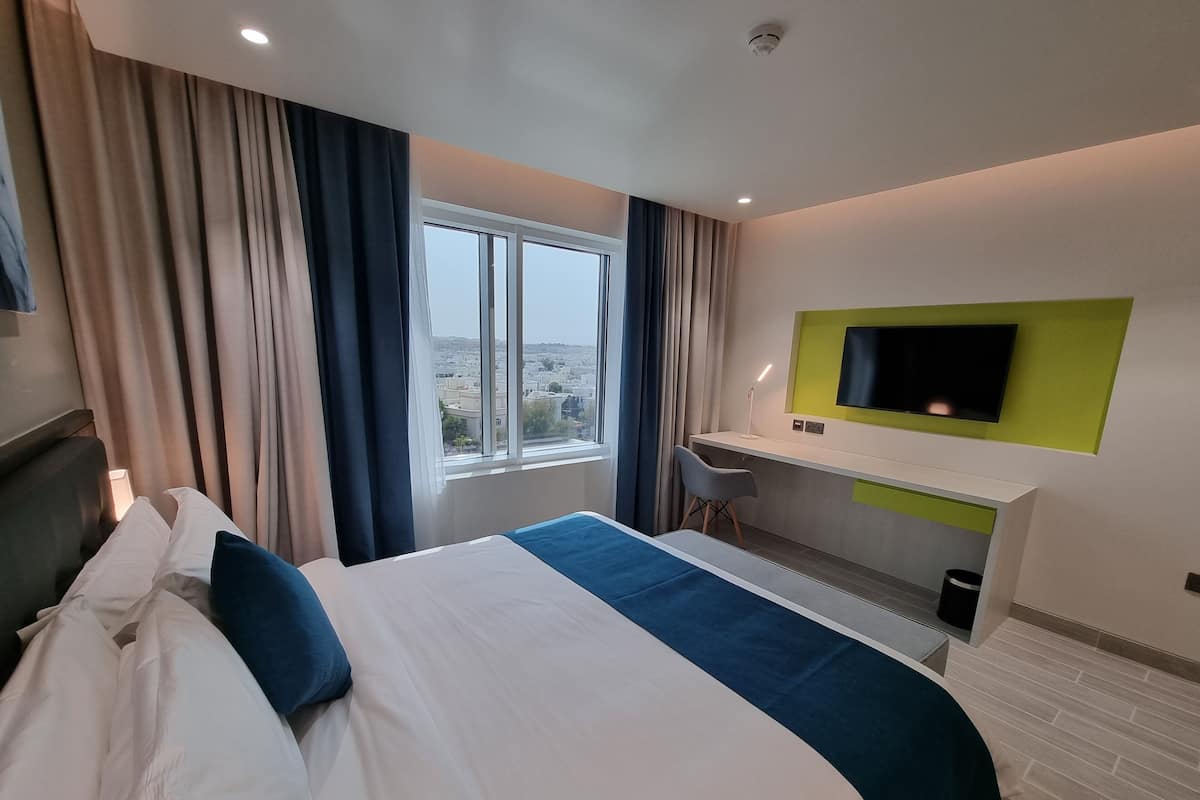 Una habitación de hotel con cama, escritorio, silla, televisión y vistas a la ciudad.