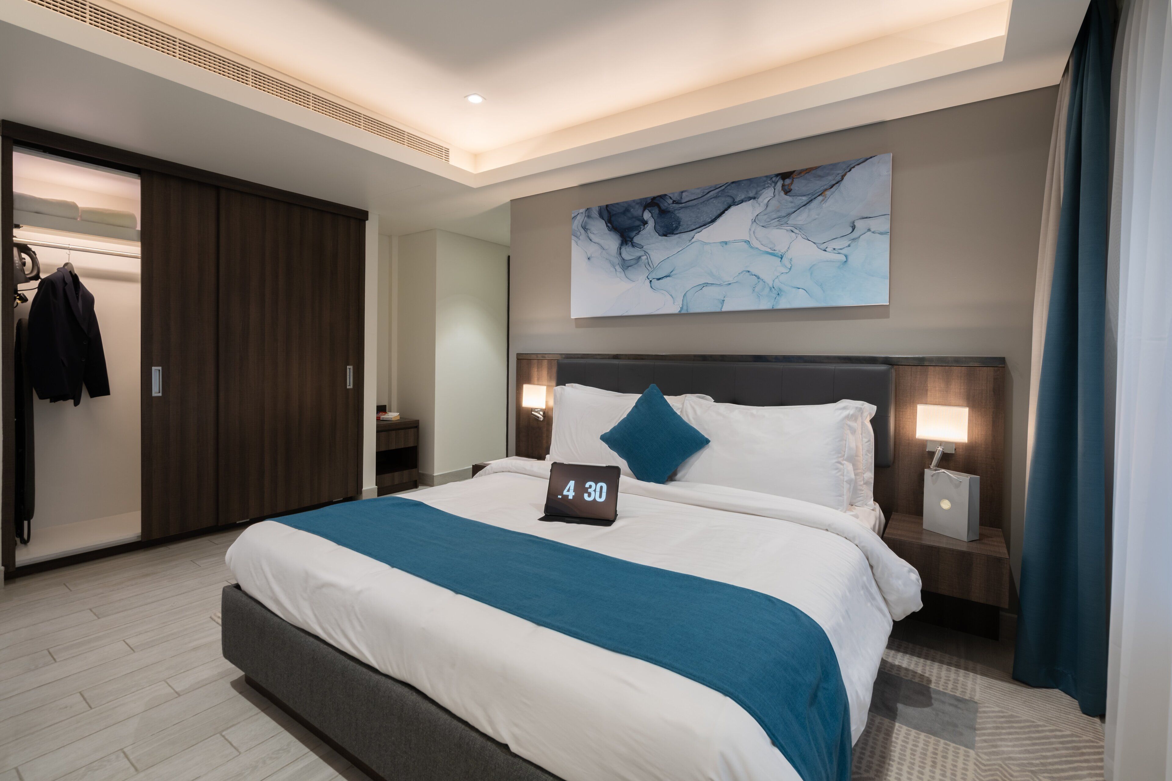 A modern hotel room with a large bed, a nightstand, a wall-mounted artwork, and a wardrobe.