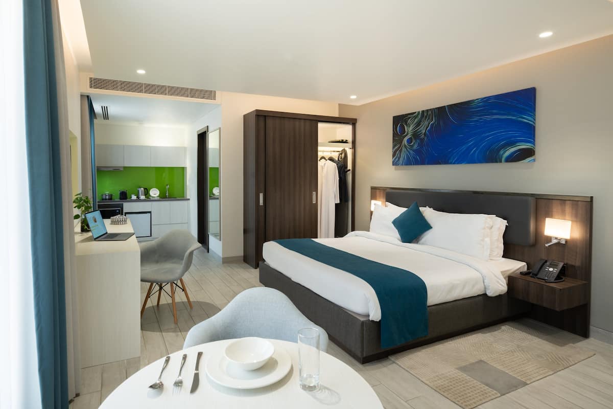A modern hotel room with a bed, bedside table, and a desk with a chair.