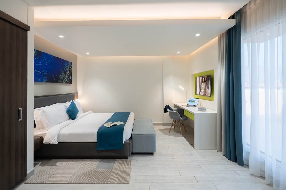 A modern hotel room with a large bed, a desk, and a computer.