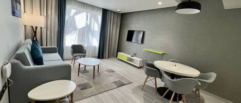 Una sala de estar moderna con un sofá, dos sillones, una mesa de centro, un televisor y una pequeña mesa de comedor.